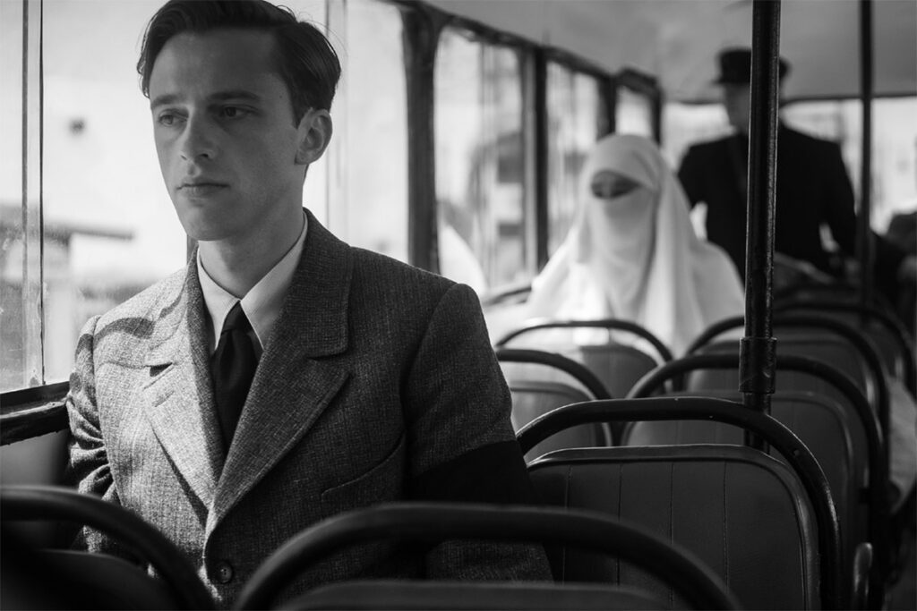 Benjamin Voisin nei panni di Meursault su un autobus, sullo sfondo una donna araba